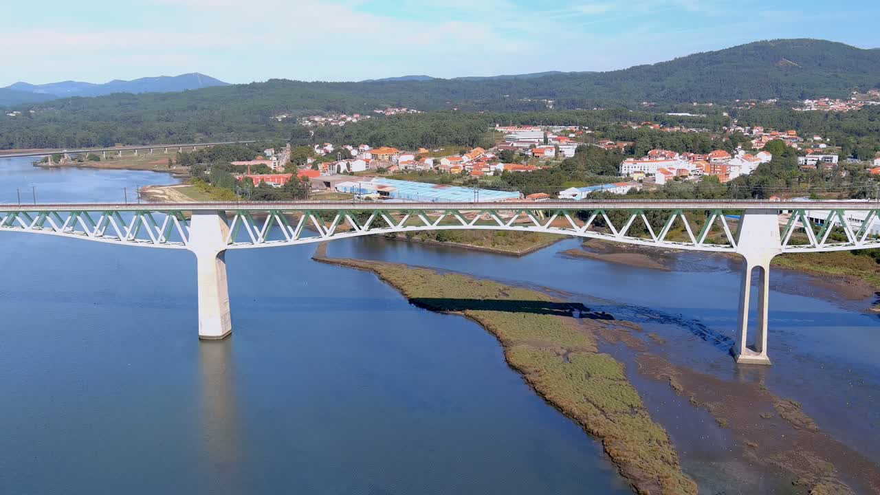 puente ferroviario sobre el río ulla, el pueblo, los edificios industriales y las montañas boscosas en el soleado cielo azul orizonte, disparo de drones que viaja hacia abajo, catoira, galicia, españa