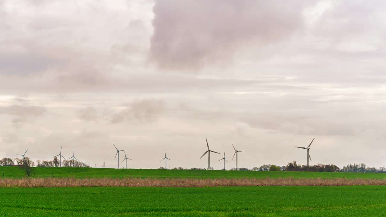 Timelapse video showcasing an expansive row of wind turbines across a serene countryside beneath a soft, cloudy sky near the North Sea coast, Lower Saxony, Germany.
