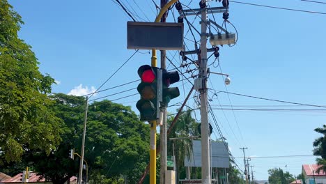 Traffic-lights-changing-from-red-to-green,-surrounded-by-a-mess-of-intertwined-electricity-cables-within-urban-city-on-sunny-blue-sky-day,-close-up-of-lights