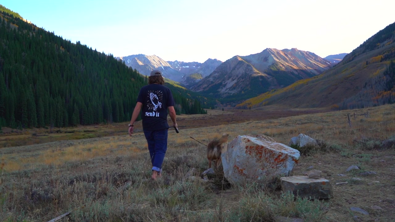 Man walking withShiba Inu dog on leash fall autumn season afternoon sunset Ashcroft ghost own valley vista Castle Conundrum Peak Elk Rocky Mountains range Colorado Aspen Snowmas landscape slide right
