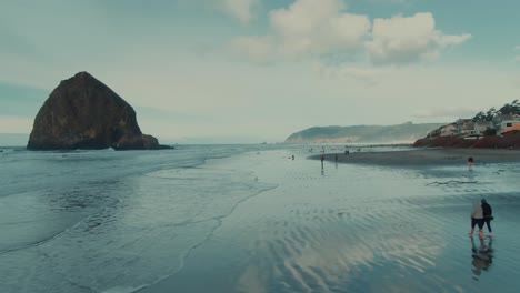 Gran-Roca-Aérea-De-4k-En-El-Océano-Cerca-De-La-Playa-Con-Gente-Caminando