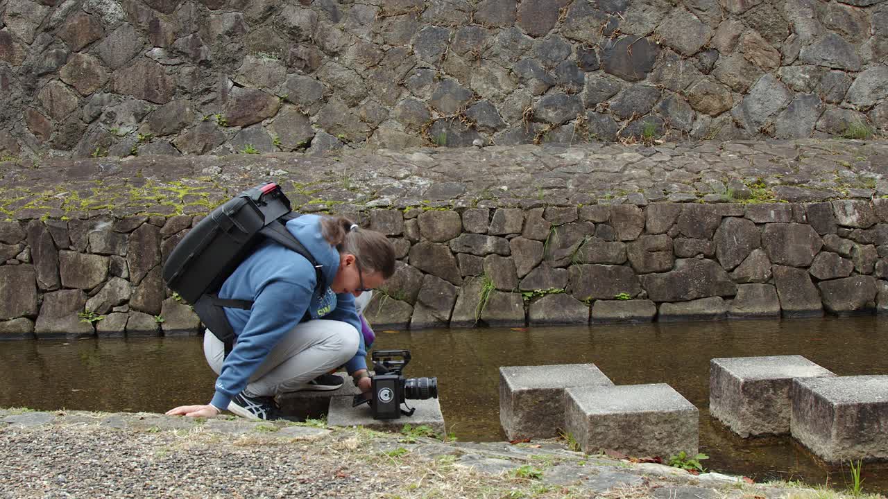Woman films low angle shot of canal with large cine camera, Kyoto