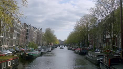 Iconic-Canal-Boats-Moored-Near-The-Port-And-Typical-Building-Architecture-In-Amsterdam,-Netherlands