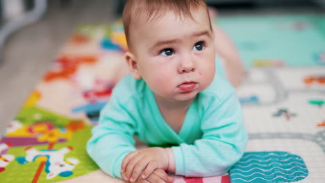 lovely baby lies on belly looking up. focused child sticks out his tongue sweetly. close up. blurred backdrop.