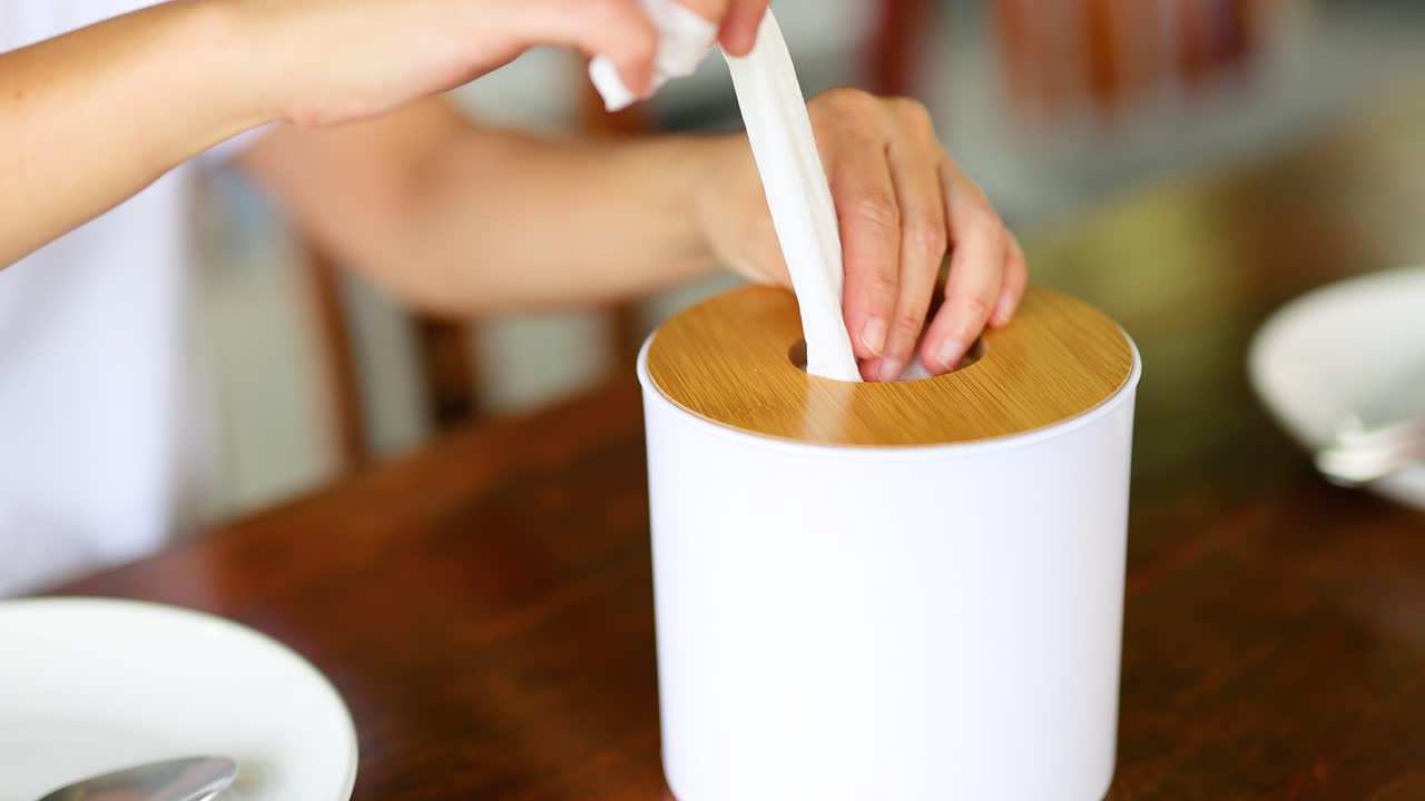 손은 잘 조명 된 식당에서 나무 테이블에 있는 세련된 디펜서에서 tissue를 당긴다