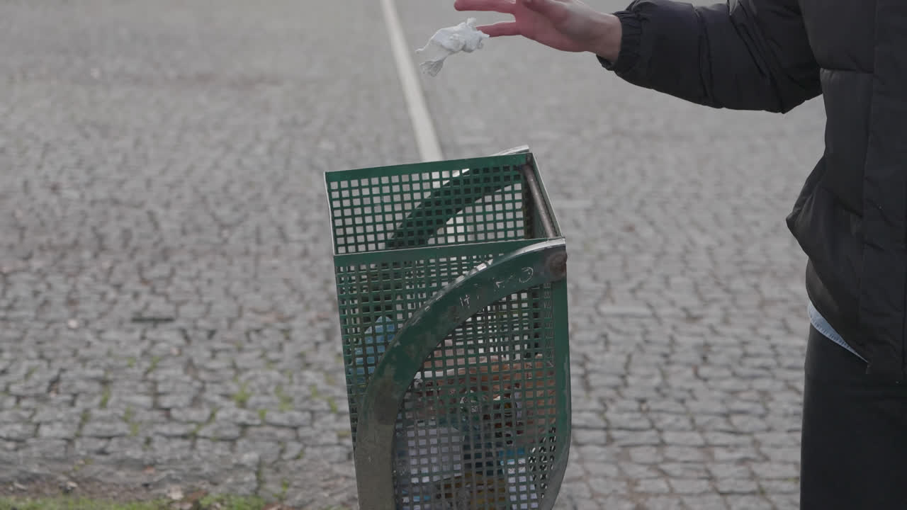 Mano che raccoglie la spazzatura da terra e la getta in un cestino pubblico.