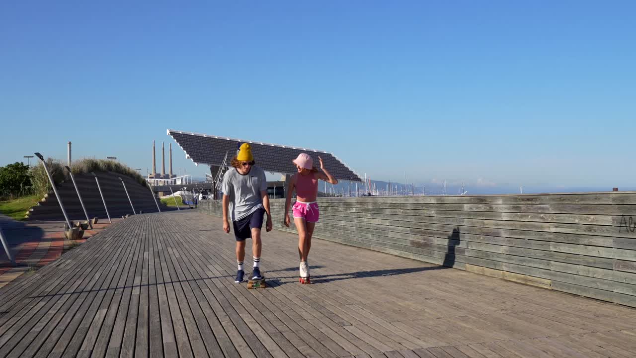 Couple skateboarding and roller skating on a sunny boardwalk