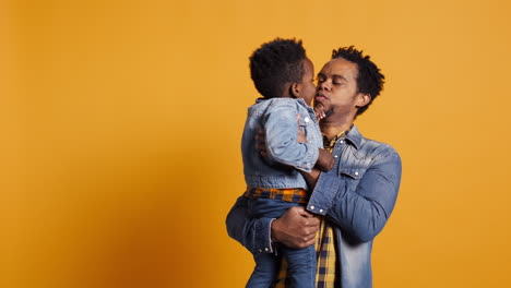 African-american-dad-caressing-and-kissing-his-adorable-baby-boy-in-studio