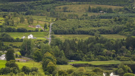 Zeitraffer-Einer-Ländlichen-Landwirtschaftslandschaft-Aus-Grünen-Feldern-Und-Wäldern-Mit-Bauernhäusern,-Vieh-Und-Verkehr-An-Einem-Bewölkten-Sommertag-In-Irland