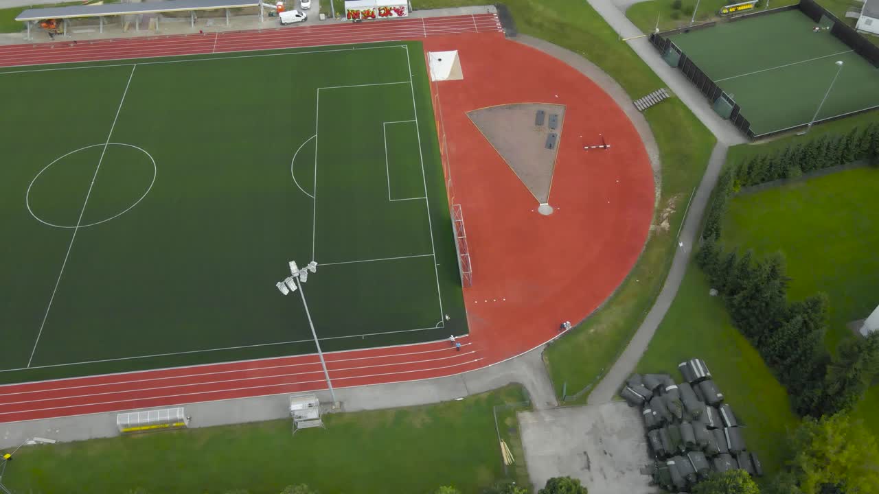 Aerial drone footage flying above a large modern green and red colored soccer stadium that has been renowated and white lines are created with white paint on the running tracks surrounding it