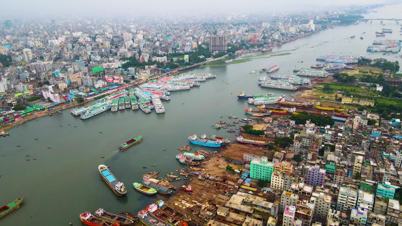 Tomada aérea de ângulo alto do porto do Rio Buriganga, exibindo navios atracados, paisagem urbana vibrante e o estaleiro de Daca, Bangladesh.
