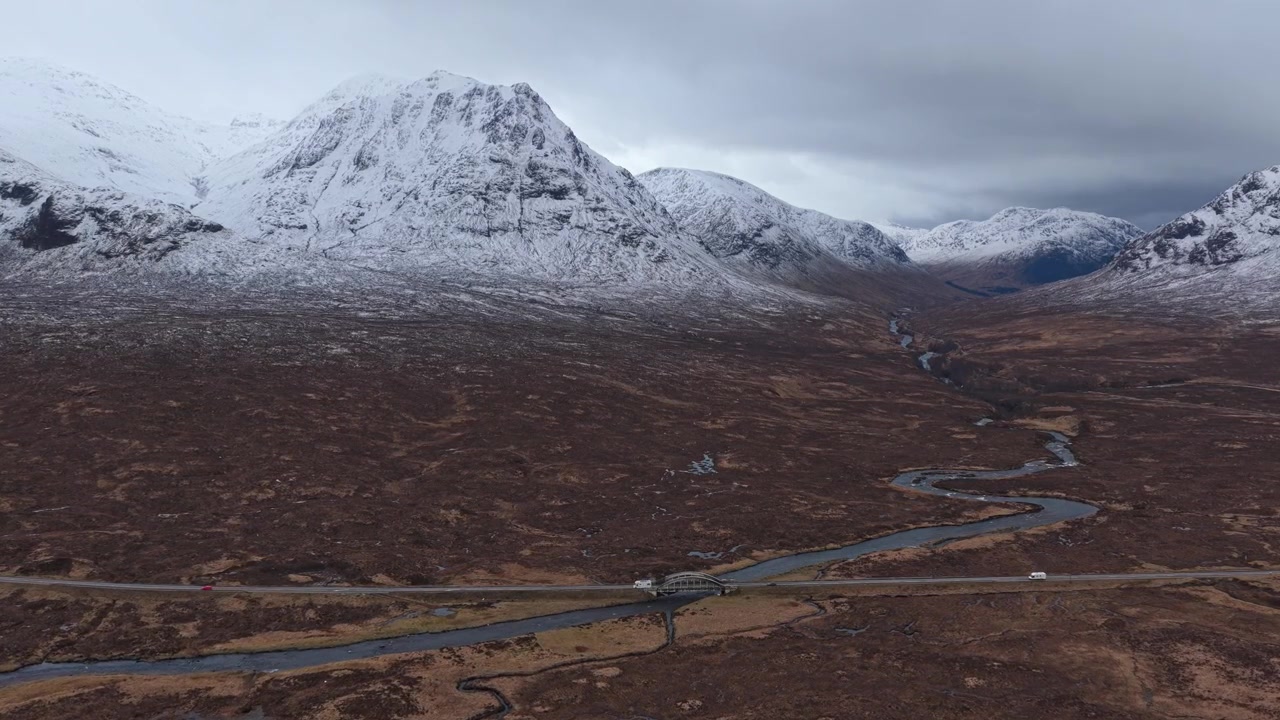 Naturskønt luftfoto af Etive-broen og vejen, med biler der kører gennem Glencoe-dalen under sneklædte bjerge.