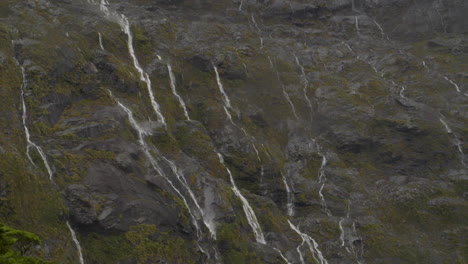 Slow-motion-static-footage-of-many-small-waterfalls-running-down-the-cliffs-after-a-storm-with-drizzle---Milford-Sound-,-New-Zealand