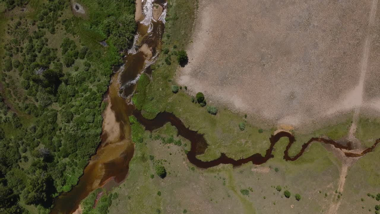 Aerial tracking follows truck on dirt road over green plains and rivers in Wind River Wilderness, Wyoming, near Big Sandy Trailhead, with mountain views in the distance
