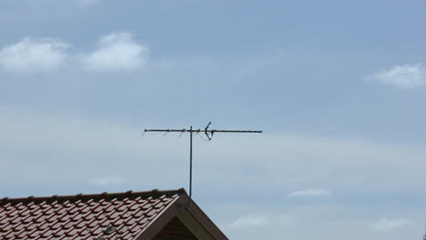 Timelapse-of-neighborhood-house-as-bids-land-on-TV-antenna-with-blue-sky-and-white-fluffy-clouds-rolling-past