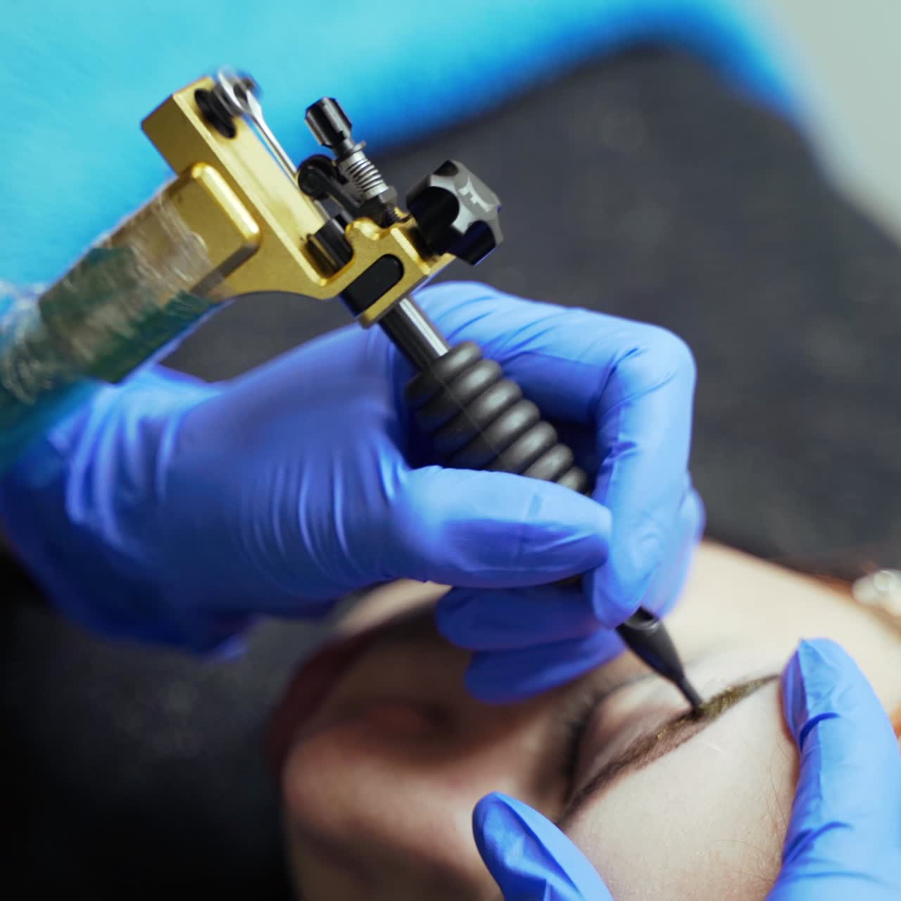 A beauty-master is doing eyebrow tattooing for the client using a special dye in the cosmetology. Blurred background. Close-up