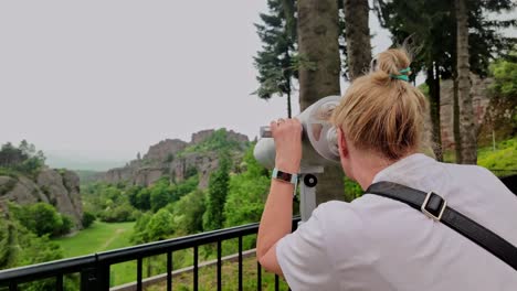 vrouw die door een observatie-telescoop kijkt naar het schilderachtige uitkijkpunt belogradchik rocks