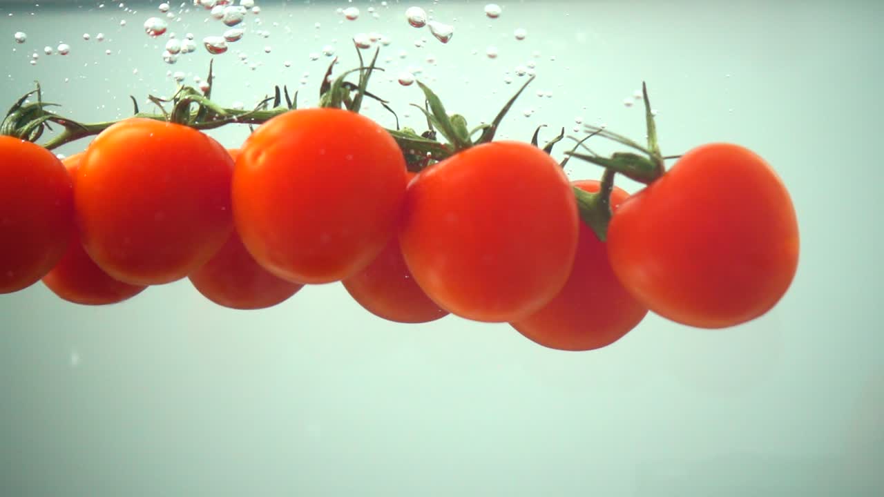 De faldende cherrytomater i vand. Slowmotion