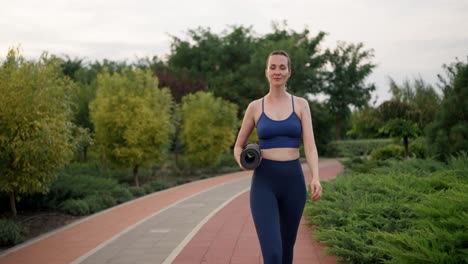 mujer caminando en el parque con una alfombra de yoga