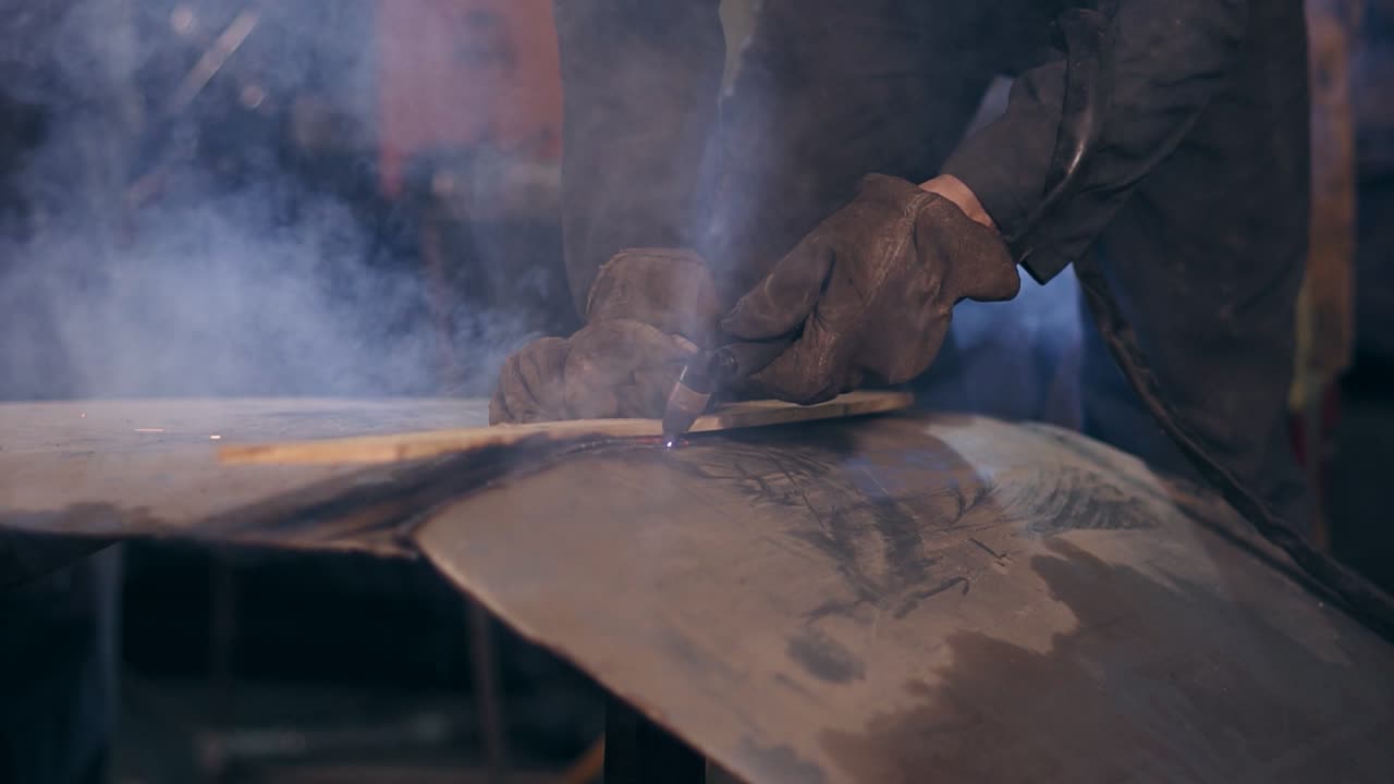 Male worker in protective workwear is cutting pieces off metal construction with oxy acetylene cutting torch