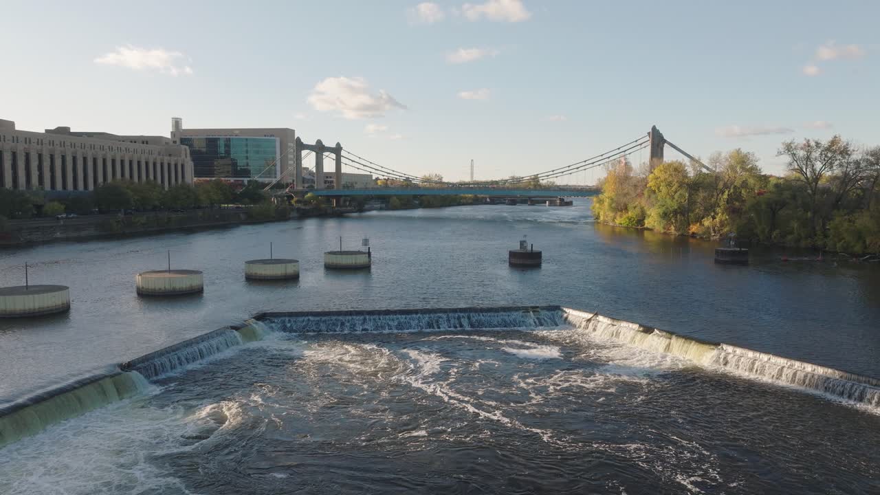Aerial drone shot of the St. Anthony Falls Dam spillway and Hennepin Avenue Bridge over the Mississippi River during fall golden hour in Minneapolis, MN