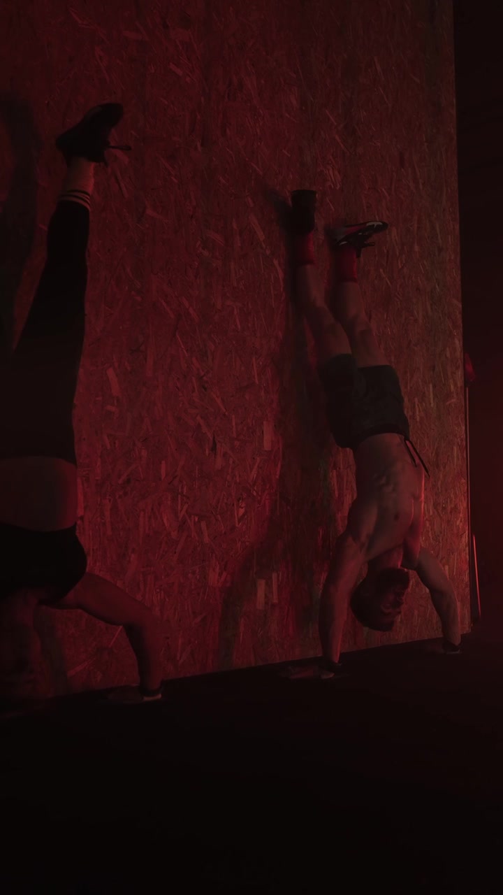 Uomo e Donna Atletici che Fanno Esercizi in Verticale in una Palestra Illuminata di Rosso