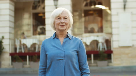 Porträtaufnahme-Einer-Schönen-Grauhaarigen-Alten-Frau-In-Blauem-Jeanshemd,-Die-Im-Freien-In-Die-Kamera-Lächelt