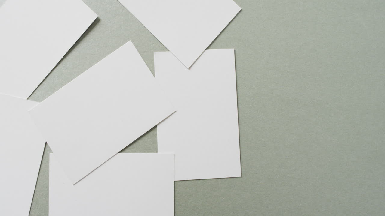 Multiple blank white business cards on green background, copy space, slow motion