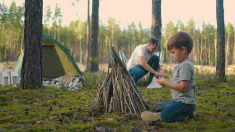 a boy of 3-4 years helps to put sticks in a campfire during a trip to the forest as a family in nature. family holiday in the woods with tents