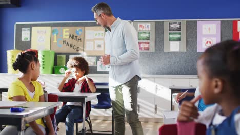 Kaukasischer-Männlicher-Lehrer,-Der-Durch-Das-Klassenzimmer-Geht-Und-Die-Übungen-Verschiedener-Kinder-überprüft