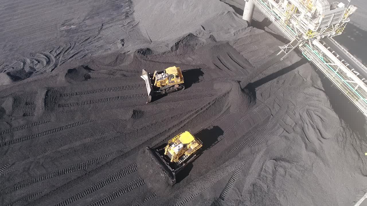 Drone shot of Coal Mine Plant, Coal coming off conveyor belt with caterpillar mining trucks moving the coal around