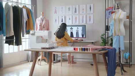 back view of a female designer designing clothes on a desktop in the studio. dress production procedure concept. cyber games clothing and designing