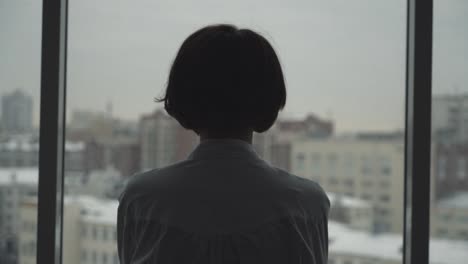 woman looking out of window at a city on a cold winter day