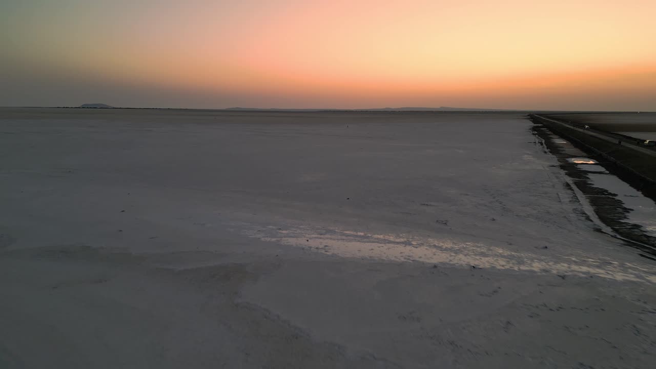 An aerial view of the Rann of Kutch, Gujarat, India reveals an endless white salt desert stretching to the horizon, glowing softly under the warm hues of a breathtaking sunset 4K