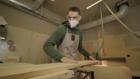 woodworker professional in mask and glasses checks wood raw, wooden plank, plywood panel