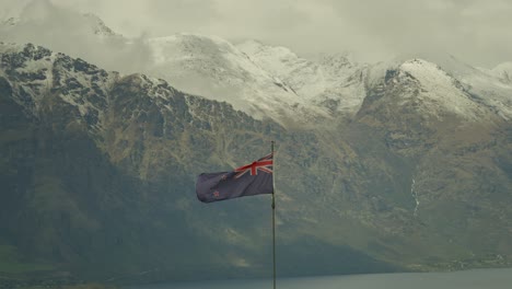 national flag of new zealand waving in wind with snowy mountains the remarkables in background