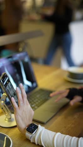 person working on laptop and phone in a cafe