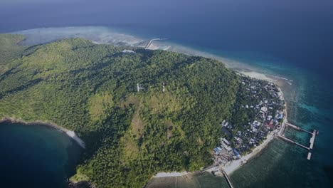toma aérea de una pequeña isla con un pequeño pueblo y un embarcadero, rodeada por el océano azul por la tarde