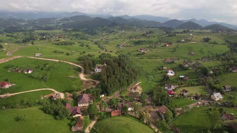 Un-Pintoresco-Pueblo-Con-Una-Iglesia-Rodeada-De-Exuberante-Vegetación-Y-Colinas,-Vista-Aérea