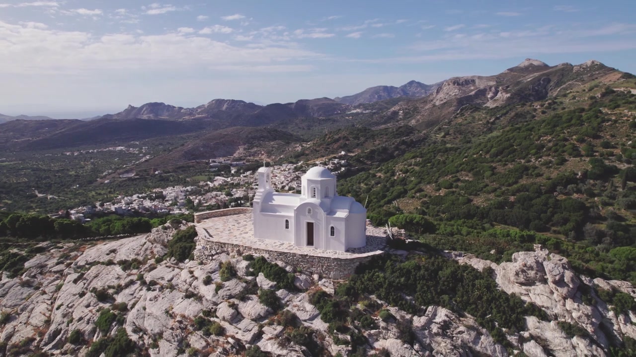Ripresa circolare con drone dall'alto della cappella del Profeta Elia sulla cima di Naxos, Grecia. Cupola cicladica imbiancata a calce contro drammatiche pareti rocciose e pendii montuosi. Aerea 4k.