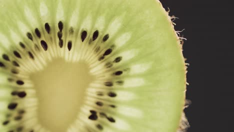 micro video of close up of slice of kiwi fruit with copy space on black background