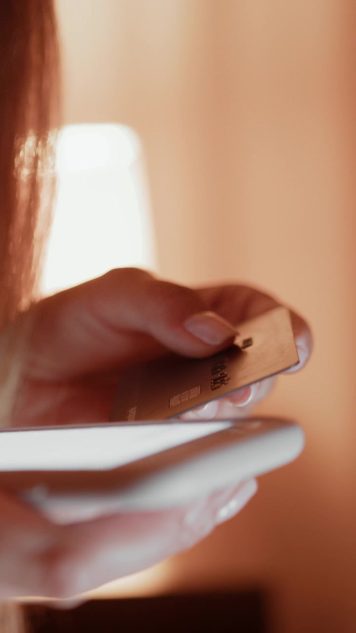 Una persona tiene una carta di credito sopra uno smartphone, pronta per effettuare un pagamento online. Questa inquadratura verticale.