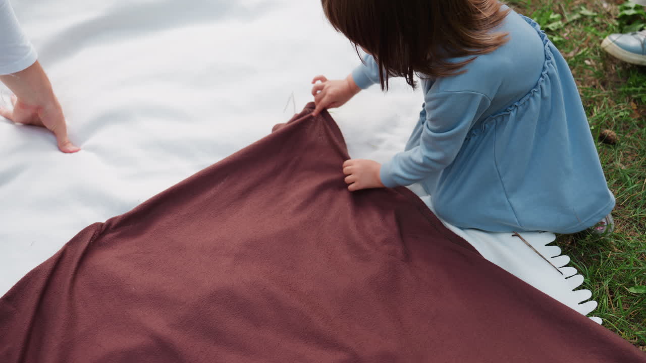 아이들이 피크닉 매트 위에 갈색 천을 놓고 흰색 매트를 덮어 팀워크를 보여주고 밝은 자연 속 숲속에서 피크닉을 준비하는 모습의 항공 뷰