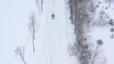 慢慢地向前飛過一條被雪覆蓋的道路,一輛灰色汽車在空中慢慢移動的下面通過