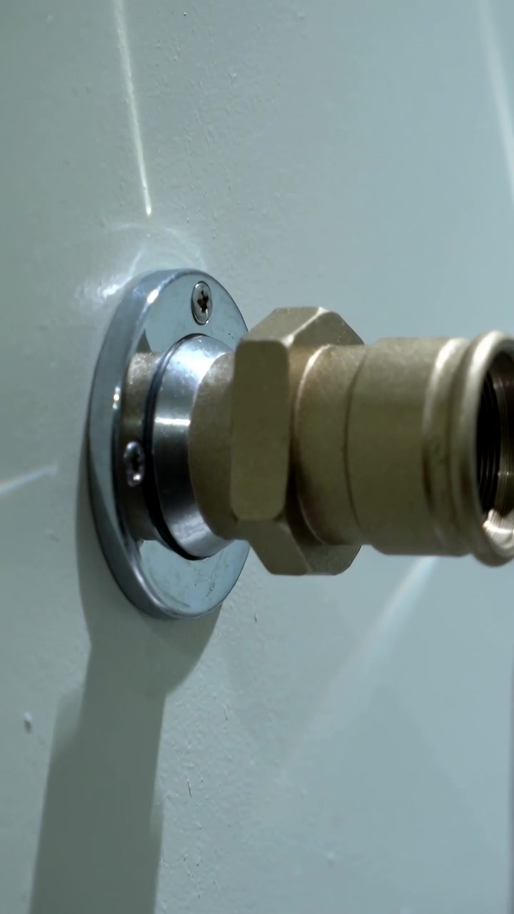 Vídeo vertical: Mão girando (fora do enquadramento) um conector hexagonal de latão na parede da lavanderia, revelando o orifício.