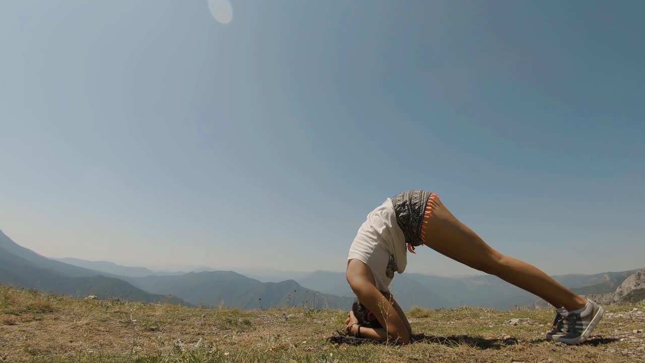 jovencita haciendo parada de cabeza de yoga en la cima de una montaña