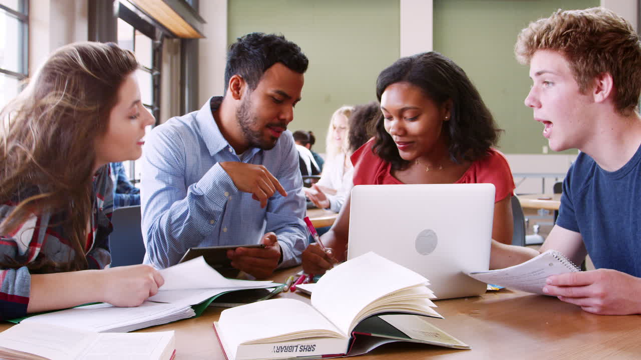 estudiantes de secundaria usando portátiles y tabletas digitales trabajando con un maestro masculino en el escritorio