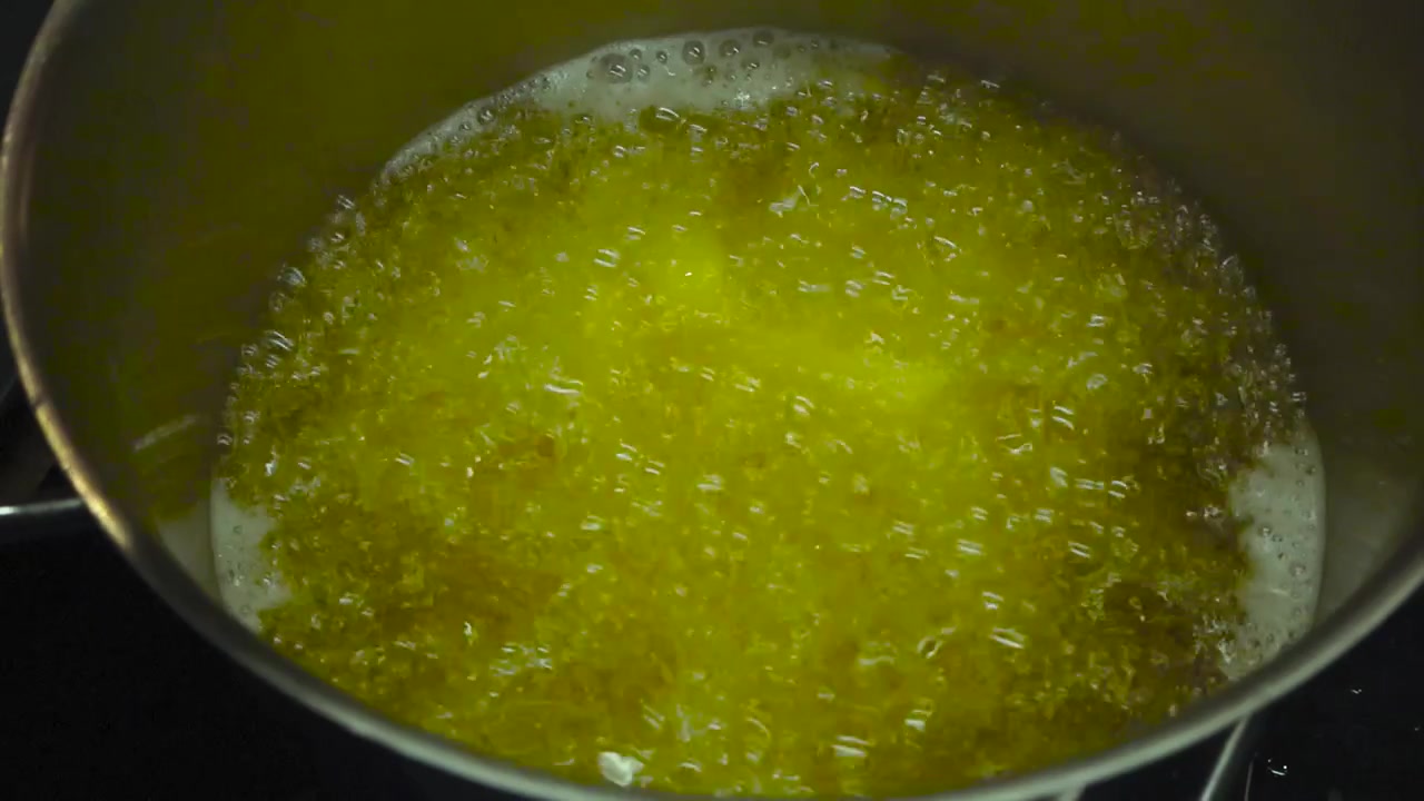 Close up or closeup footage of home made golden yellow french fries cooking in vibrant bubbly and hot oil that is bubbling and foaming in slow motion in a metallic gray pot on a stove indoors.
