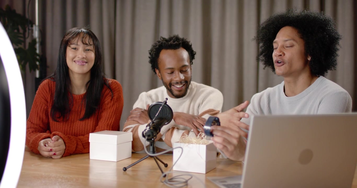 Diverse coworkers unboxing and demoing device on table in studio with smartphone starting recording