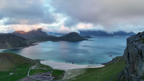 Drone passes man on cliff revealing stunning view of Haukland beach in midnight sun landscape
